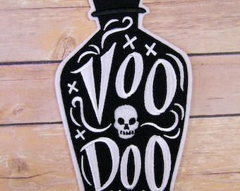 May include: Black and white embroidered patch of a bottle with a skull and the text "Voodoo" on it.