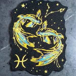 Peut inclure: Patch thermocollant brodé représentant le signe du zodiaque des Poissons avec deux poissons dorés et bleus nageant sur un fond de nuit étoilée noire.