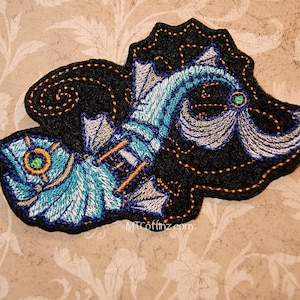 Peut inclure: Patch brodé représentant une créature marine bleue et argentée avec des accents dorés sur un fond noir. La créature a une grande nageoire et une longue queue. Le patch est entouré d'une bordure cousue dorée.
