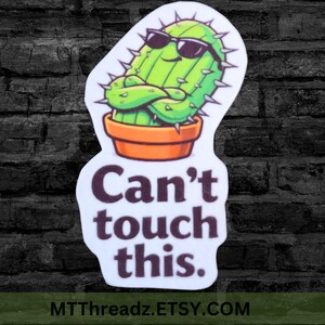 May include: A sticker featuring a cartoon cactus wearing sunglasses and an orange pot. The cactus has its arms crossed and is surrounded by thorns. The text "Can't touch this" is below the cactus.
