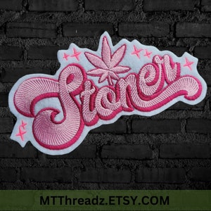 May include: An embroidered patch featuring the word Stoner in a cursive pink font with a white outline. The design includes a central cannabis leaf icon and several small four-pointed star accents in pink thread against a white fabric backing.