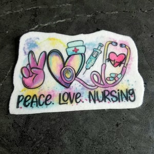 May include: A white sticker with a peace sign, a heart, a stethoscope, a syringe, and pills. The text "Peace Love Nursing" is written below the image.