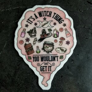 May include: Pink and white sticker with the text "It's a witch thing you wouldn't get it" and illustrations of a witch's hat, cauldron, potion bottles, and other witchy items.