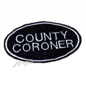 Peut inclure: Écusson brodé ovale noir avec du texte blanc qui dit "COUNTY CORONER".