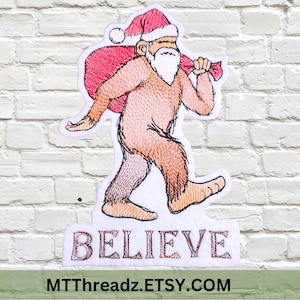 May include: Embroidered patch featuring a Bigfoot character in a Santa hat carrying a sack. The patch is in shades of brown, pink, and red, with the word "BELIEVE" embroidered below. The patch is on a white background.