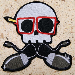 May include: Embroidered patch featuring a white skull wearing red-rimmed glasses and a yellow pencil behind the skull. The skull is wearing black headphones with grey mouse-shaped earpieces.