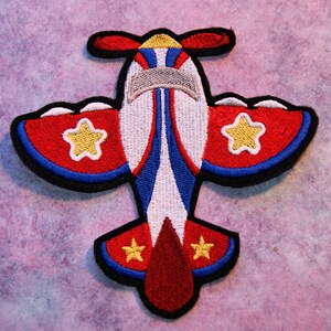 May include: A red, white, and blue airplane applique with yellow stars. The airplane has a propeller on top and a black outline.