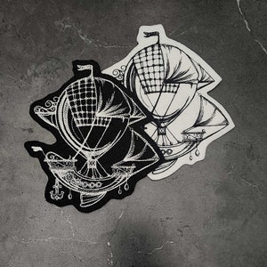 May include: Two embroidered patches featuring a vintage airship design. One patch is black with white detailing, and the other is white with black detailing. The airships have intricate line art, with a basket, sails, and decorative elements.