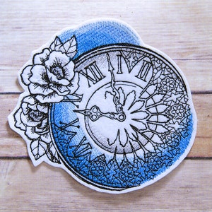 May include: An embroidered patch featuring a clock face with Roman numerals and a floral design. The clock face is surrounded by a blue and white floral pattern. The patch is ideal for adding a touch of vintage charm to any project.