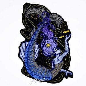 May include: An embroidered patch depicting a mermaid with purple hair and a blue tail. The mermaid is surrounded by a swirling pattern of gold and black.