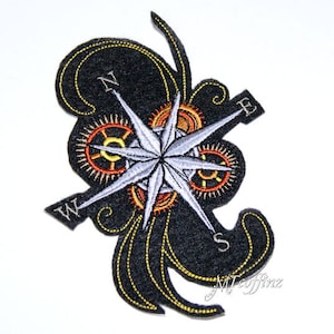 May include: Embroidered iron-on patch featuring a compass rose with gears and a swirling design. The compass points are labeled N, S, E, and W. The patch is black with gold and orange accents.