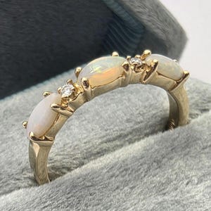 Peut inclure: Une bague en or ornée de trois opales ovales et de deux petits diamants ronds intercalés. Les pierres sont disposées en ligne sur le dessus de l'anneau en or poli, présenté dans un écrin à bijoux doublé de velours gris.