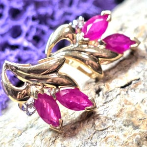 May include: A pair of gold-toned earrings featuring marquise-cut, vibrant pink gemstones and small, clear accent stones. The earrings have a leaf-like design, with the gemstones arranged to resemble petals.