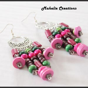 May include: A pair of silver earrings with pink, green, and brown wooden beads. The earrings feature a decorative silver circle at the top and dangle from a silver hook.
