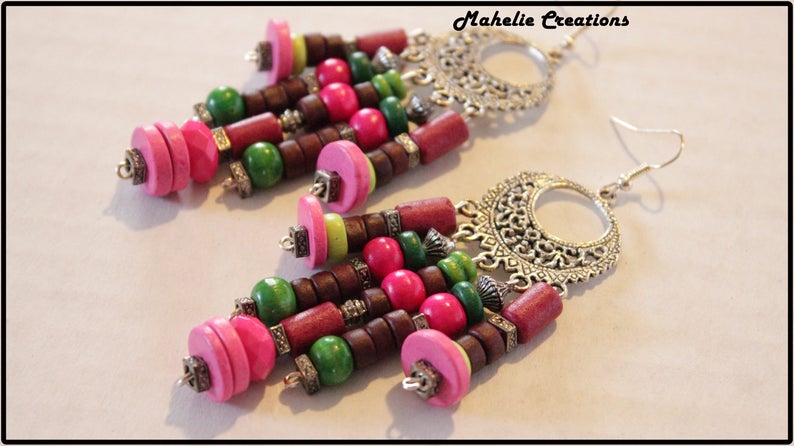 May include: A pair of dangle earrings with a silver filigree design and colorful wooden beads. The beads are pink, green, and brown. The earrings are approximately 3 inches long.