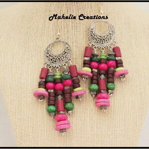 May include: Silver filigree earrings with a cascade of pink, green, and brown wooden beads. The earrings are labeled "Mahelie Creations".