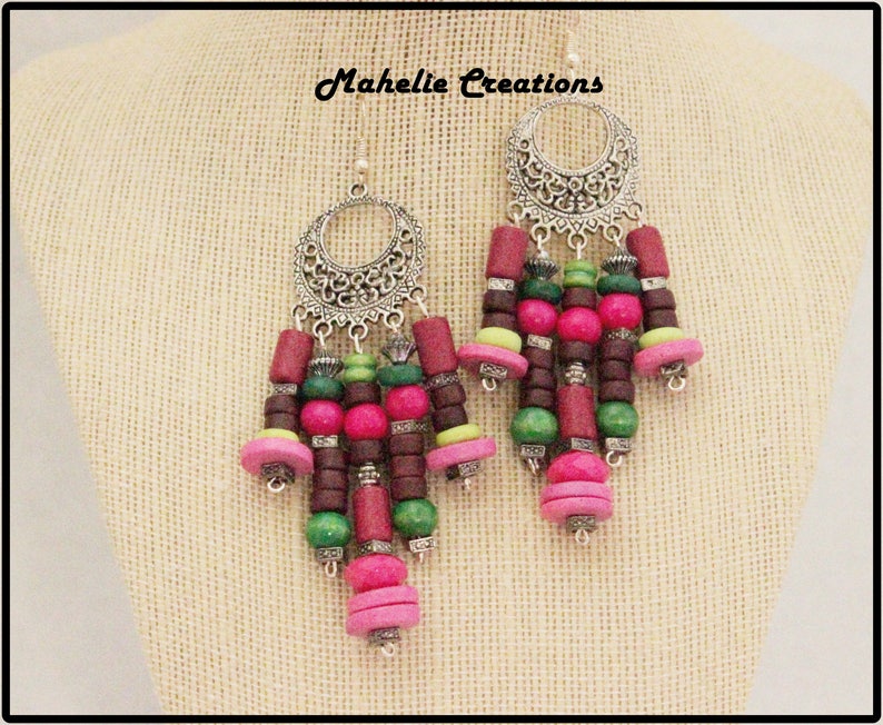 May include: Silver filigree earrings with a cascade of pink, green, and brown wooden beads. The earrings are labeled "Mahelie Creations".
