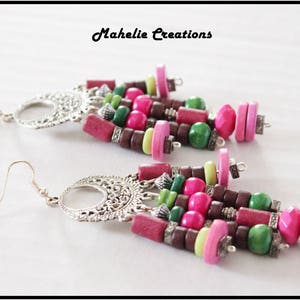 May include: A pair of long, dangling earrings with silver metal accents and colorful wooden beads. The beads are pink, green, brown, and light green. The earrings are labeled "Mahelie Creations".