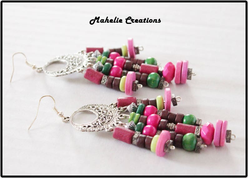 May include: A pair of long, dangling earrings with silver metal accents and colorful wooden beads. The beads are pink, green, brown, and light green. The earrings are labeled "Mahelie Creations".