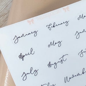 May include: A sheet of white stickers with the months of the year written in elegant black cursive script. The months include January, February, April, May, July, August, and October.