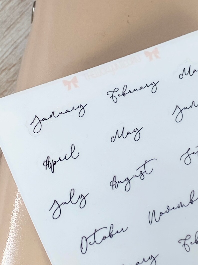 May include: A sheet of white stickers with the months of the year written in elegant black cursive script. The months include January, February, April, May, July, August, and October.
