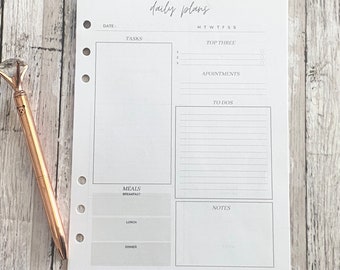 May include: A white daily planner sheet with the words "daily plans" at the top. The planner includes sections for tasks, appointments, to-dos, and meals. A rose gold pen with a diamond-shaped top rests on the left side.