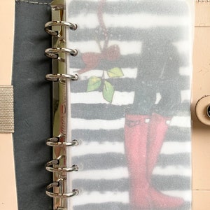 May include: A planner insert with a black and white striped background and a graphic of red rain boots. The insert is labeled "inbox" at the top and is held in a ring binder.