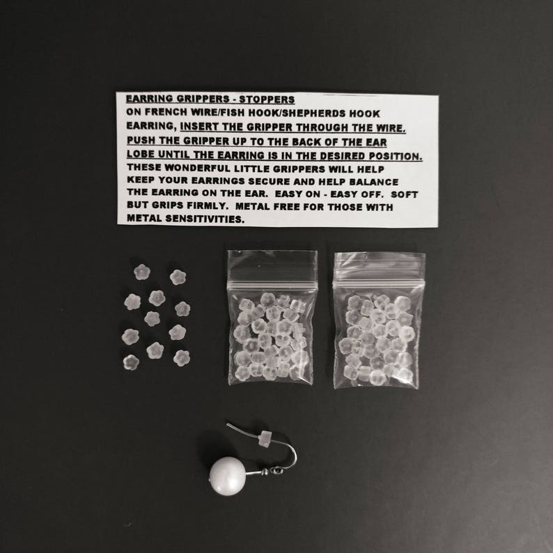 May include: A set of clear plastic earring grippers in two small bags and a single earring with a pearl. The text on the card reads: "Earring Grippers - Stoppers on French Wire/Fish Hook/Shepherds Hook Earring, Insert the gripper through the wire. Push the gripper up to the back of the ear lobe until the earring is in the desired position. These wonderful little grippers will help keep your earrings secure and help balance the earring on the ear. Easy on - Easy off. Soft but grips firmly. Metal free for those with metal sensitivities."