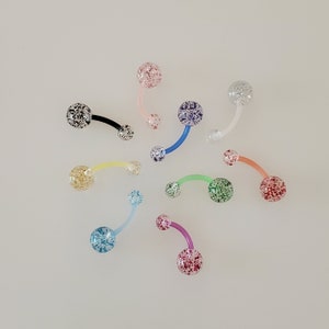May include: Assortment of colorful belly button rings with glitter accents. The rings are made of clear plastic and have a variety of colors, including pink, blue, green, yellow, and purple.