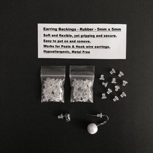May include: Two clear plastic bags filled with small, clear rubber earring backs. There are also 10 individual earring backs laid out on a black surface. The text on the white card reads: "Earring Backings - Rubber - 5mm x 5mm Soft and flexible, yet gripping and secure. Easy to put on and remove. Works for Posts & Hook wire earrings. Hypoallergenic, Metal Free"