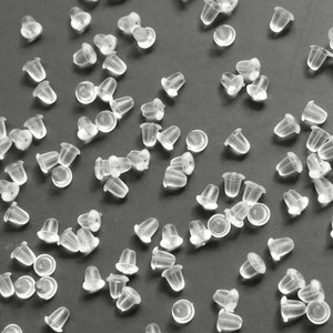 May include: A large quantity of clear plastic earring backs scattered on a gray surface.