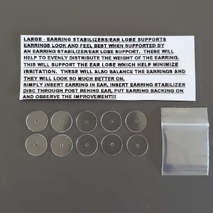 May include: A pack of clear plastic earring stabilizers or ear lobe supports. The pack includes 8 stabilizers and a small clear plastic bag. The text on the white card reads: "LARGE - EARRING STABILIZERS/EAR LOBE SUPPORTS EARRINGS LOOK AND FEEL BEST WHEN SUPPORTED BY AN EARRING STABILIZER/EAR LOBE SUPPORT. THESE WILL HELP TO EVENLY DISTRIBUTE THE WEIGHT OF THE EARRING. THIS WILL SUPPORT THE EAR LOBE WHICH HELP MINIMIZE IRRITATION. THESE WILL ALSO BALANCE THE EARRINGS AND THEY WILL LOOK SO MUCH BETTER ON. SIMPLY INSERT EARRING IN EAR, INSERT EARRING STABILIZER DISC THROUGH POST BEHIND EAR, PUT EARRING BACKING ON AND OBSERVE THE IMPROVEMENT!!"