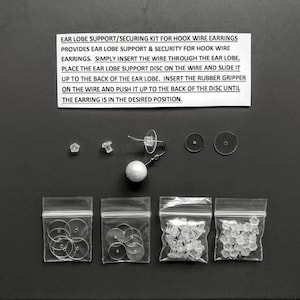 May include: A set of clear plastic earlobe support discs and rubber grippers for hook wire earrings. The set includes a small bag of 10 discs, a small bag of 10 grippers, and a larger bag of 20 grippers. The image also shows a pair of earrings with a pearl bead and a hook wire.