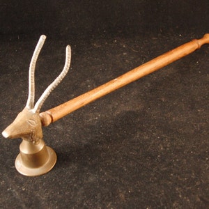 May include: A wooden handled candle snuffer with a brass animal head design. The animal has two long horns and a detailed face.
