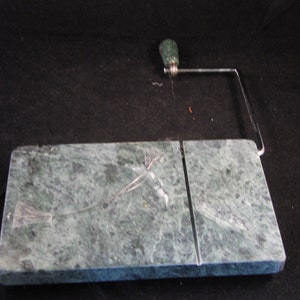 May include: Green marble cheese board with a built-in wire cheese slicer. The slicer has a green handle and a silver metal frame.