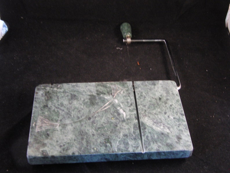 May include: Green marble cheese board with a built-in wire cheese slicer. The slicer has a green handle and a silver metal frame.