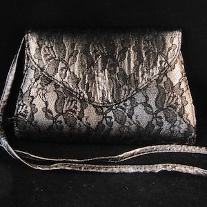 May include: A black and silver clutch purse with a lace pattern and a long strap.