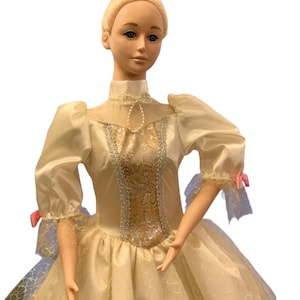 May include: A porcelain doll dressed in a white and gold ballerina costume with a silver crown. The doll has blonde hair and blue eyes.