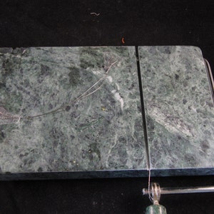 May include: A green marble cheese board with a built-in wire cheese cutter. The board is divided into two sections.