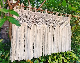 May include: White crocheted curtain with a lace trim and fringe. The curtain is hanging from a wooden rod.