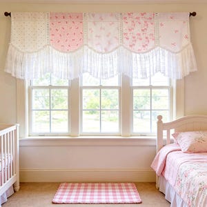 May include: A nursery scene with a white cot and a bed with a floral patterned duvet cover. A window is decorated with a valance in white and pink patterns. A pink and white checked rug is on the floor.