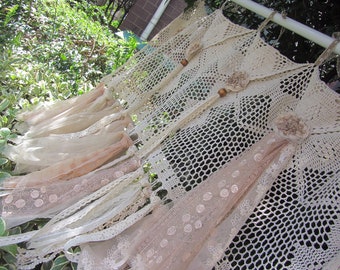 May include: A white crocheted curtain with a delicate lace trim and brown wooden beads. The curtain is hanging from a white rod and is decorated with a brown crocheted flower.