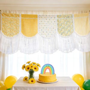 May include: A celebratory scene featuring yellow and green balloons, a yellow cake with a rainbow decoration, and a vase of sunflowers. A patterned yellow and white valance hangs above a window, creating a bright atmosphere.