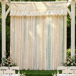 May include: A decorative backdrop featuring vertical strips of pastel-colored fabric and white lace hanging from a horizontal rod. The curtain includes a ruffled valance at the top with intricate lace detailing in shades of pink, blue, and yellow.