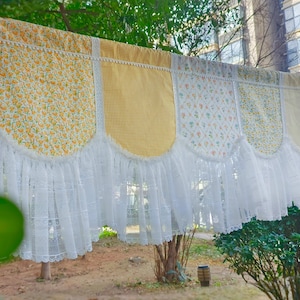 May include: A decorative valance with a patchwork design, featuring floral, gingham, and solid fabric panels in yellow and white. The valance has a scalloped edge and is trimmed with white lace, creating a vintage, cottagecore aesthetic.