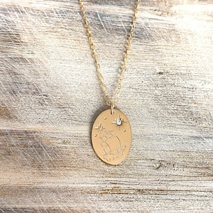 May include: A gold necklace with a pendant featuring a ship sailing under a star with a small diamond accent. The pendant is oval shaped and has a textured surface.