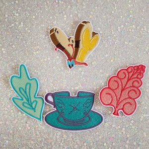 May include: Embroidered patches featuring a butterfly, a teacup, and two leaf designs. The butterfly has brown and yellow wings with a red and blue body. The teacup is teal with a purple handle and saucer. The leaves are teal and red.