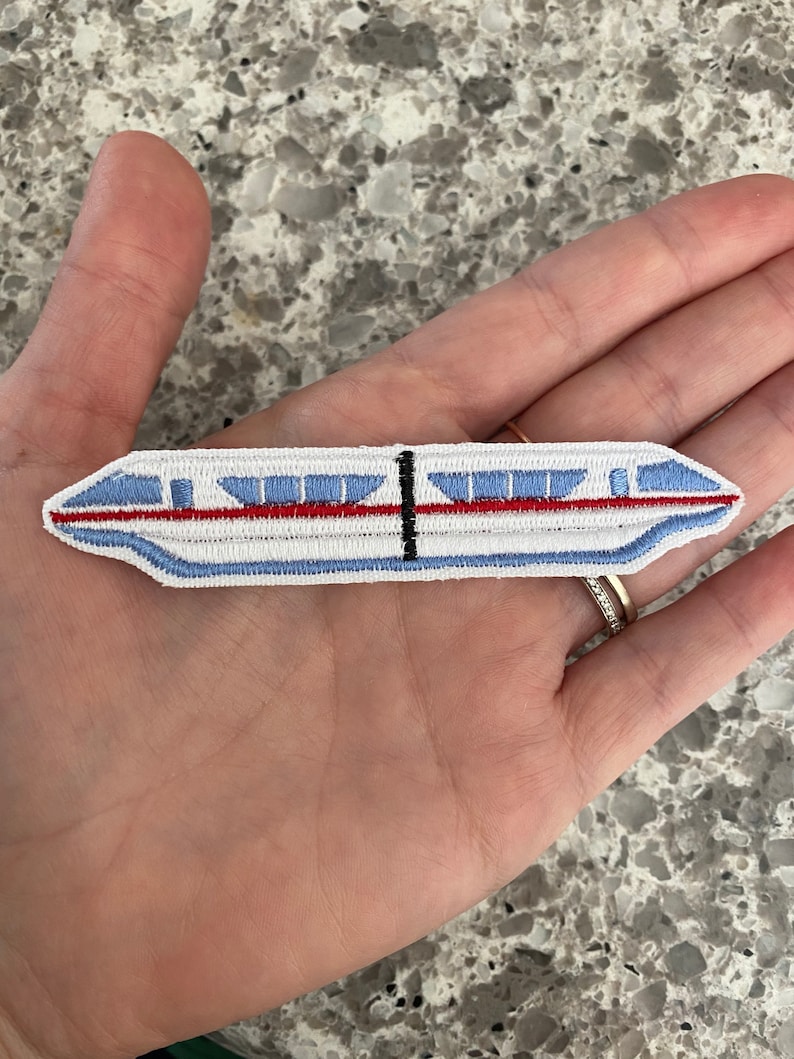 May include: White embroidered patch of a monorail train with red and blue details.