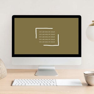 May include: A computer screen displaying a motivational quote in white text on a brown background. The quote reads "You are held by grace" repeated five times.