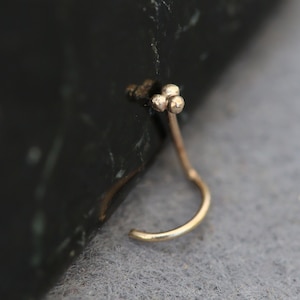 May include: A gold nose ring with a small, three-ball design at the top.